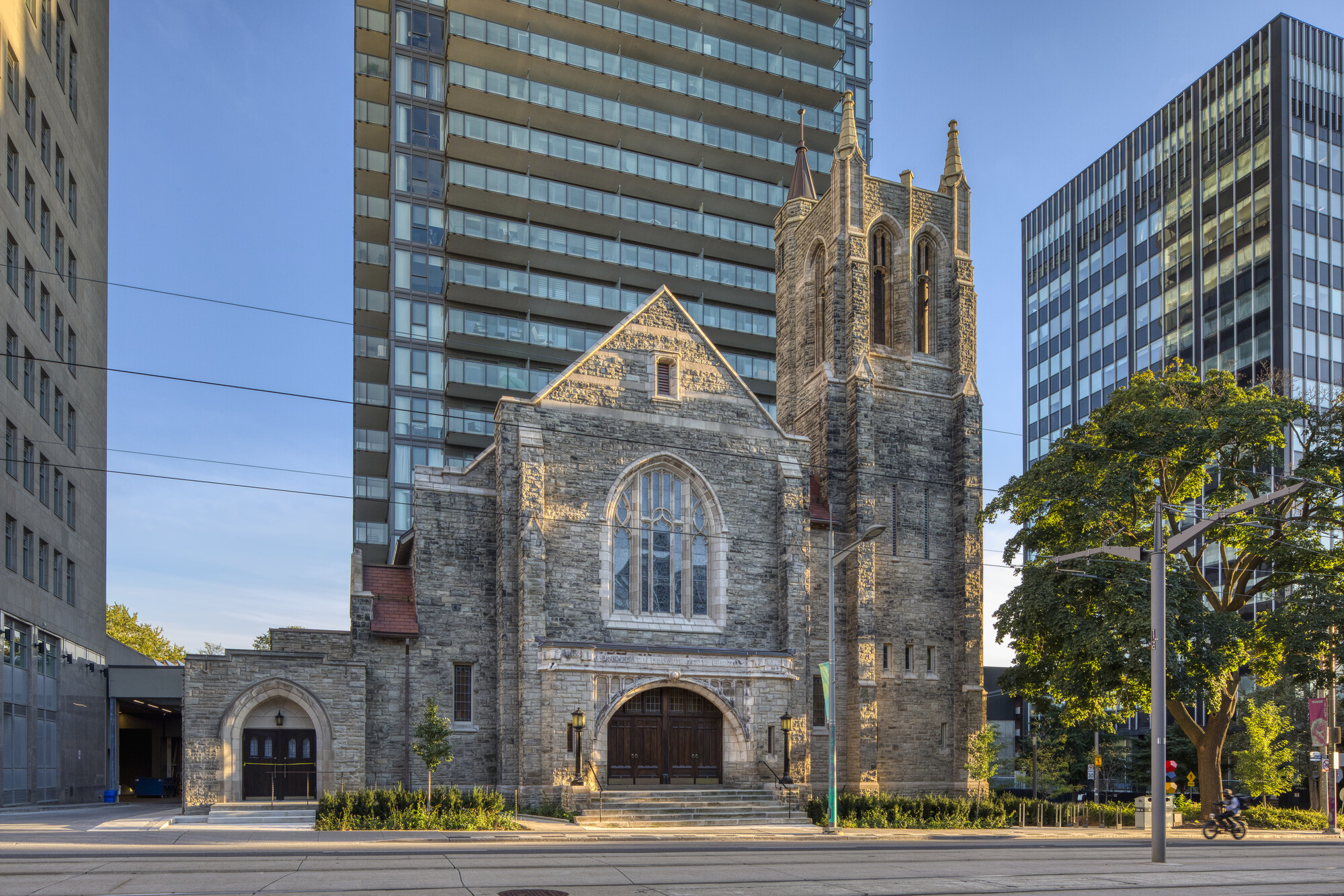 Street-facing view of Deer Park Church with its stone façade and central tower framed by modern high-rises in the background.