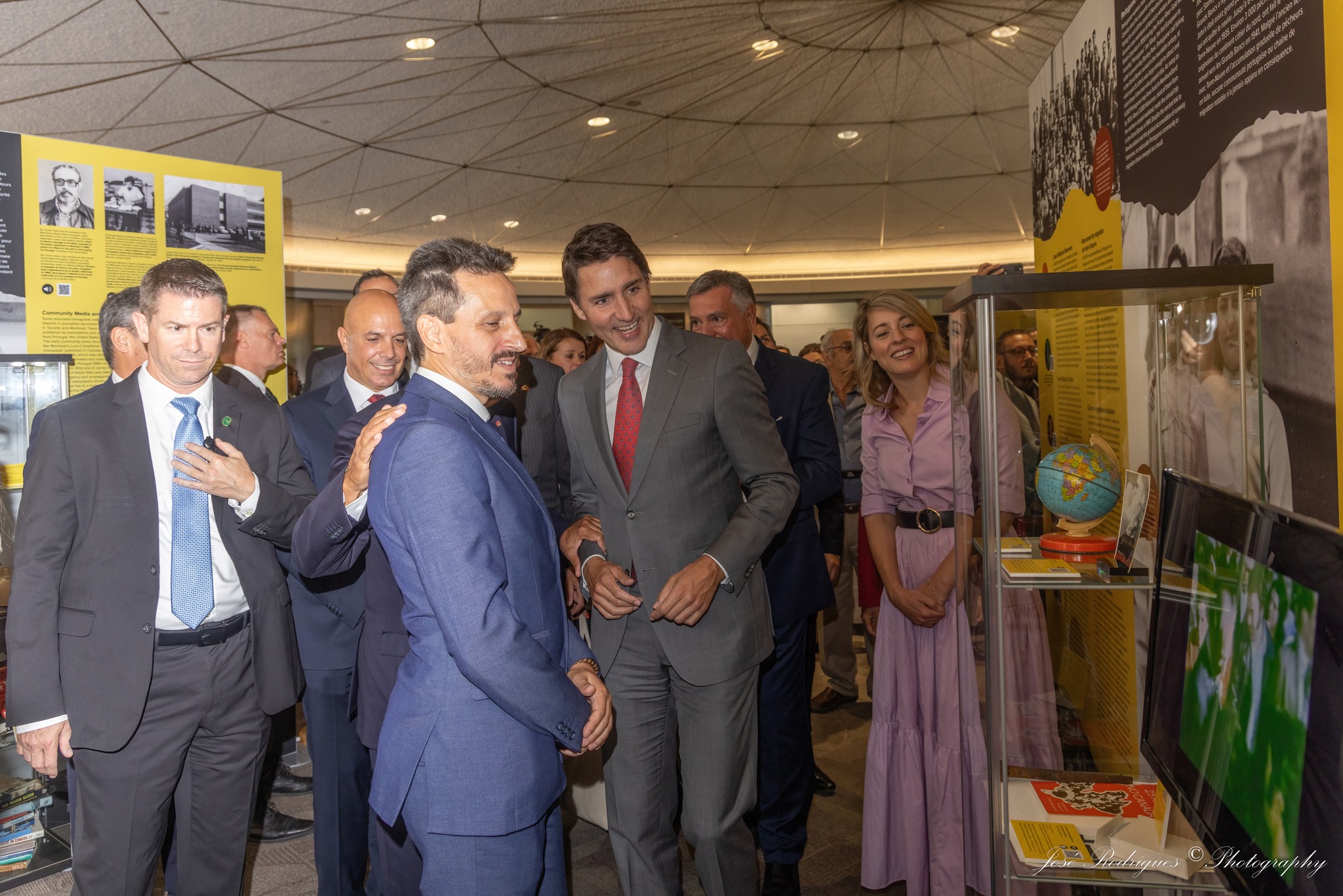 A group of people admiring an exhibit case with yellow text panels in the background.