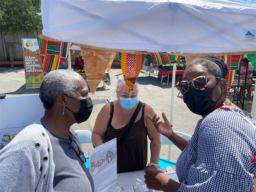a group of three women wearing face masks standing underneath a Jay Pitter Placemaking tent.