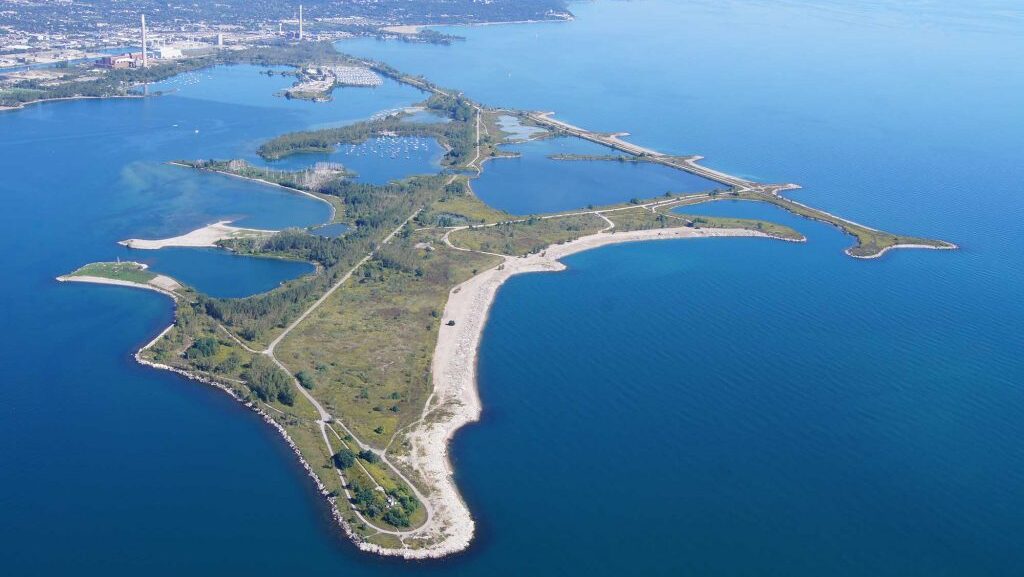 Colour aerial photo of a sinuous landform approximately 5 kilometres in length in a large body of water. It is connected to a mainland by a narrow neck of land.