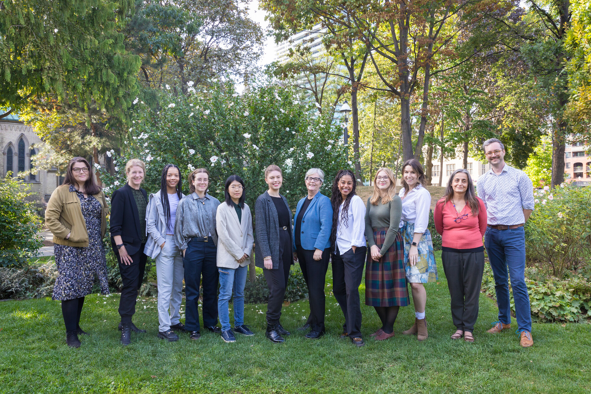 Photo of a group of people smiling and facing the camera. There are trees in the background.