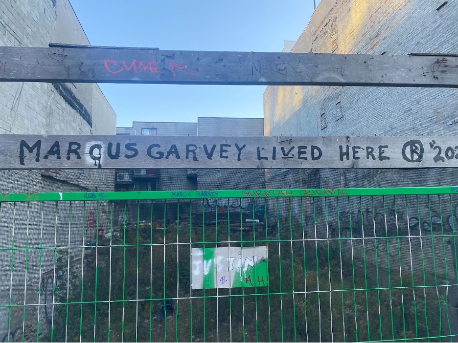 Black marker on scaffolding outside of a construction site. The text reads: “MARCUS GARVEY LIVED HERE”.