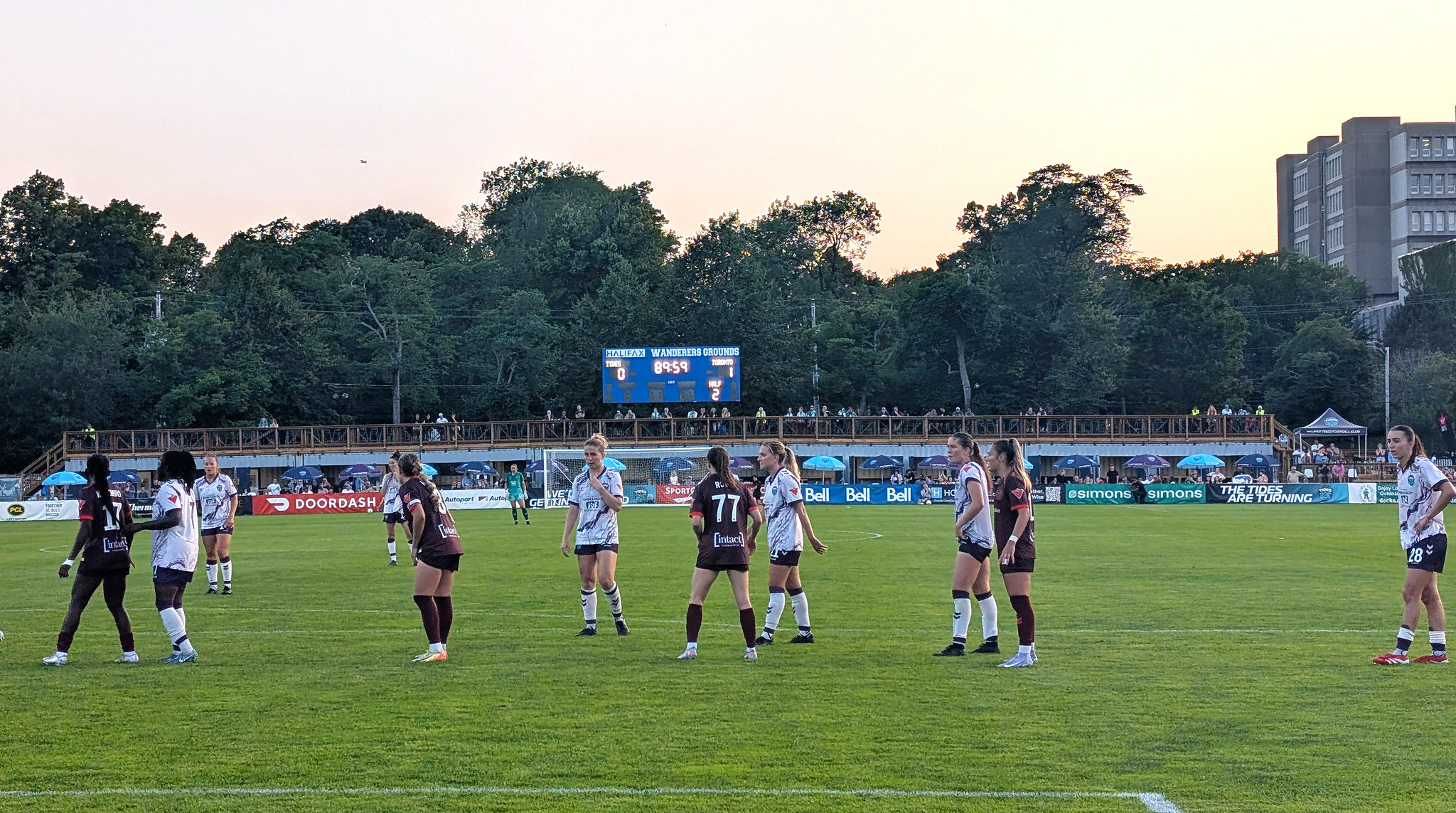 Soccer players on opposing teams playing on a field. Spectators can be seen in the background.