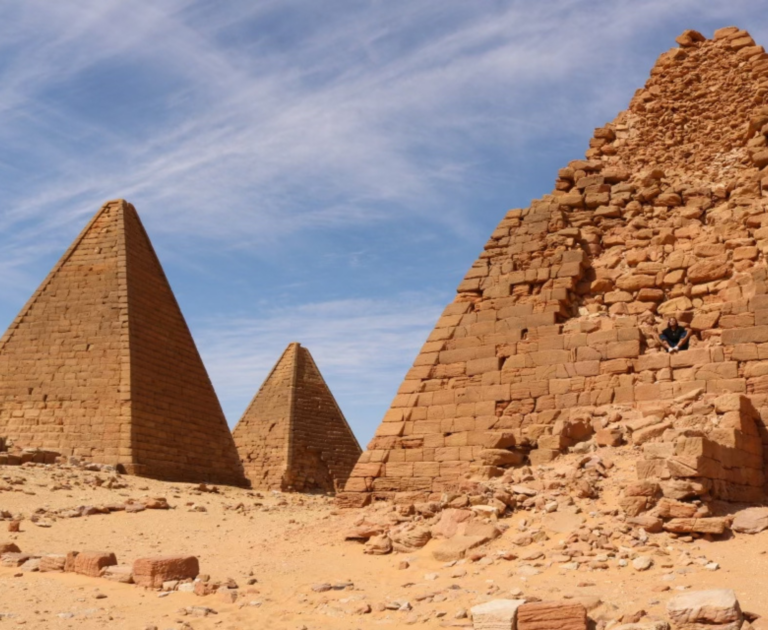 Three orange-brick pyramids are featured in the picture against a cloudy blue sky.