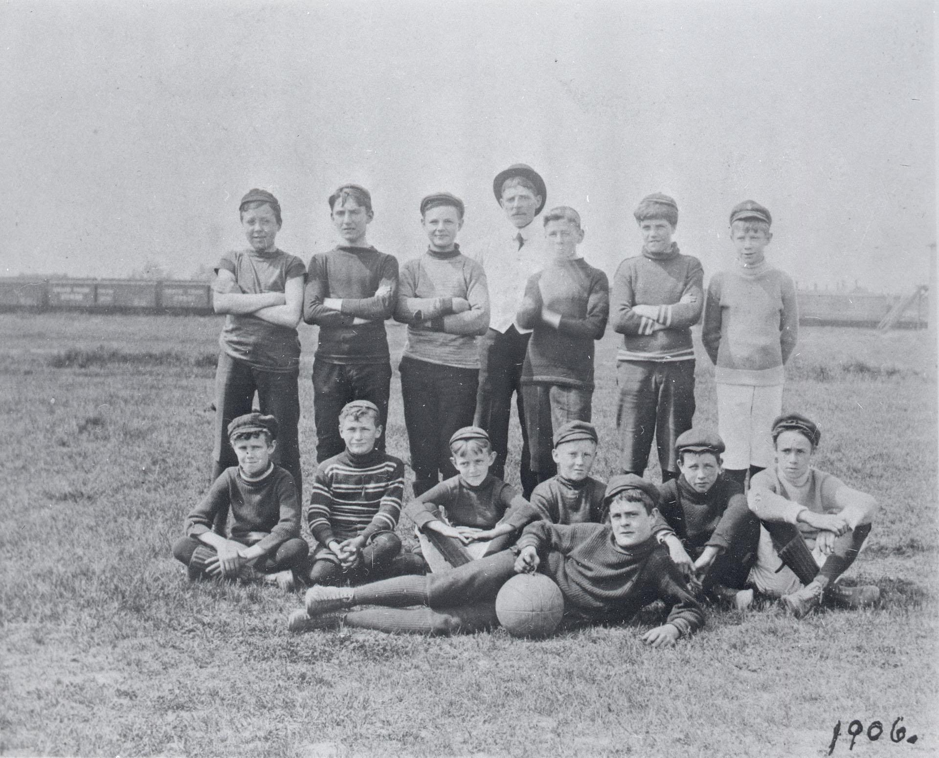 Two rows of fourteen young people pose for a picture. In the front row, one person is posing with a soccer ball.