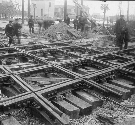 A black and white photograph of men at work laying down railway tracks in 1920's style clothing. They are creating the diamond railway crossings in the West end of Toronto.
