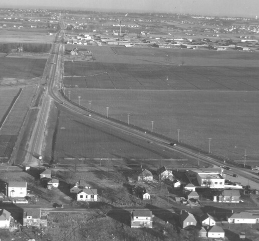 Black and white slightly aerial photograph looking east along Eglinton Avenue East. The area is mostly agricultural with a scattering of houses. A factory is visible in the middle distance.