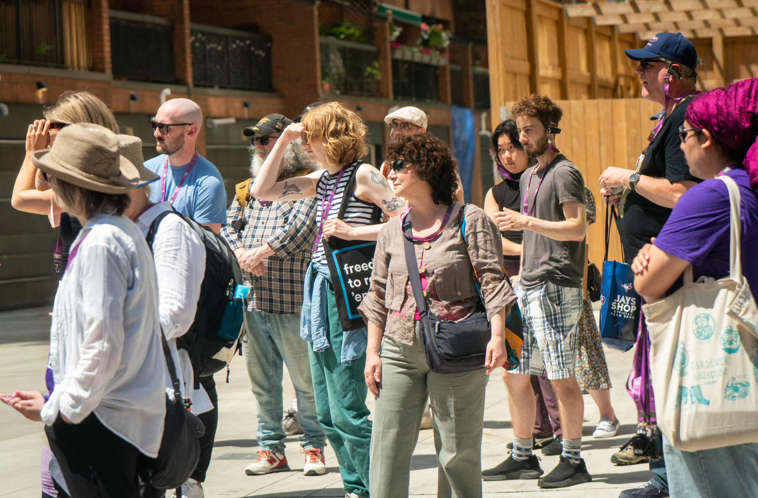 A group of people stand on concrete and look attentively to the left of the image.