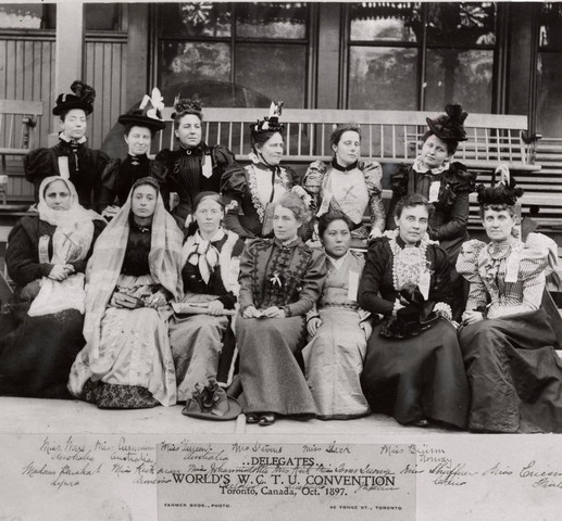 Black and white photo of a group of women in long dresses of all kinds sitting on the steps of a building.  The text at the bottom of the photo reads, "..Delegates.. World's W. C. T. U. Convention Toronto, Canada, Oct. 1897. Farmer Bros., Photo 92 Yonge Street". The names of the women are scribbled in pencil over top of the caption and across the bottom of the image.