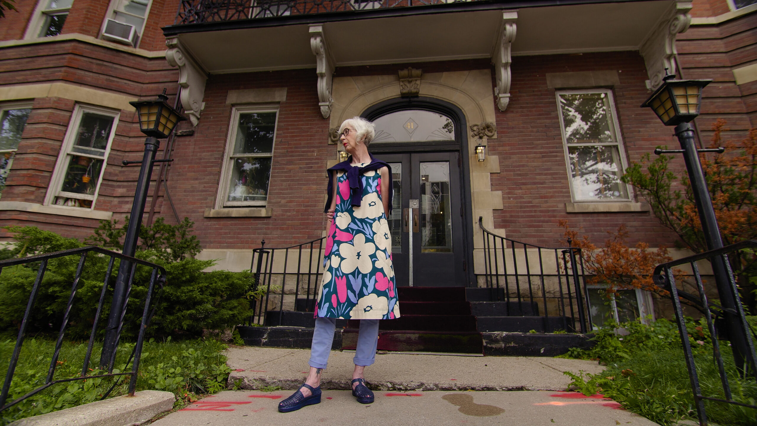 A woman wearing a floral colourful dress standing in front of an old building entrance.