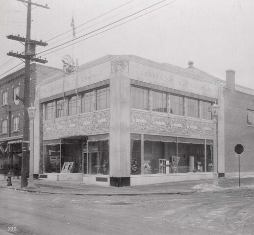 Black and white photo of a two-storey building on a street corner. On the road beside the building is a 1930s car.