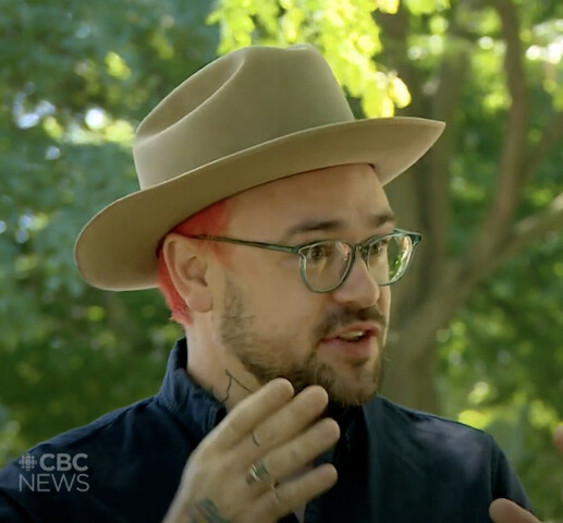 Screenshot of television interview with Morgan Cameron Ross. Man is being interviewed outside, wearing a beige brimmed hat, glasses and a navy suit jacket. A watermark logo in the bottom left corner is of the CBC logo and reads "CBC NEWS". Grey text box on the far right of the image reads "Morgan Cameron Ross / Old Toronto Series"