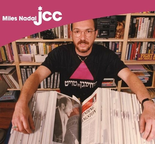 Advertisement for an exhibit. Title text reads "Twice Blessed / A Toronto Jewish Queer community in the 1980s and '90s through the collections of Johnny Abush" In bold pink lettering are the dates of the exhibition "July 4 - August 5, 2019". The photo is of a man holding a very large book with photos and newspaper articles inside. The background is a bookshelf.