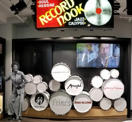 A room full of music memorabilia . On the back wall there are drums and a tv set. On the left wall are record art and on the right are various pieces of music ephemera.