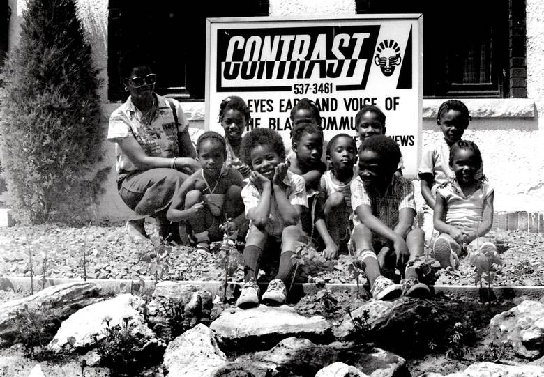 A group of children and an adult pose for a photograph. Behind them is a large poster reading: "Contrast."