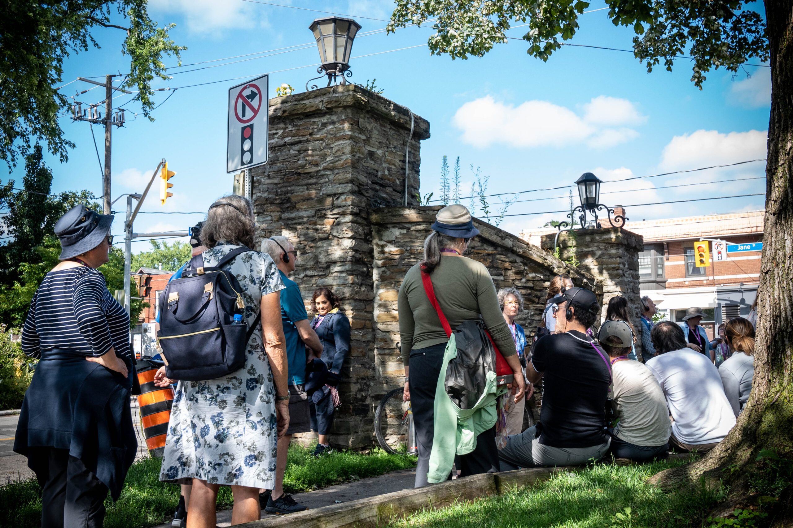 A group of people standing on the side of a road. An old stone gate's remnants are still visible.
