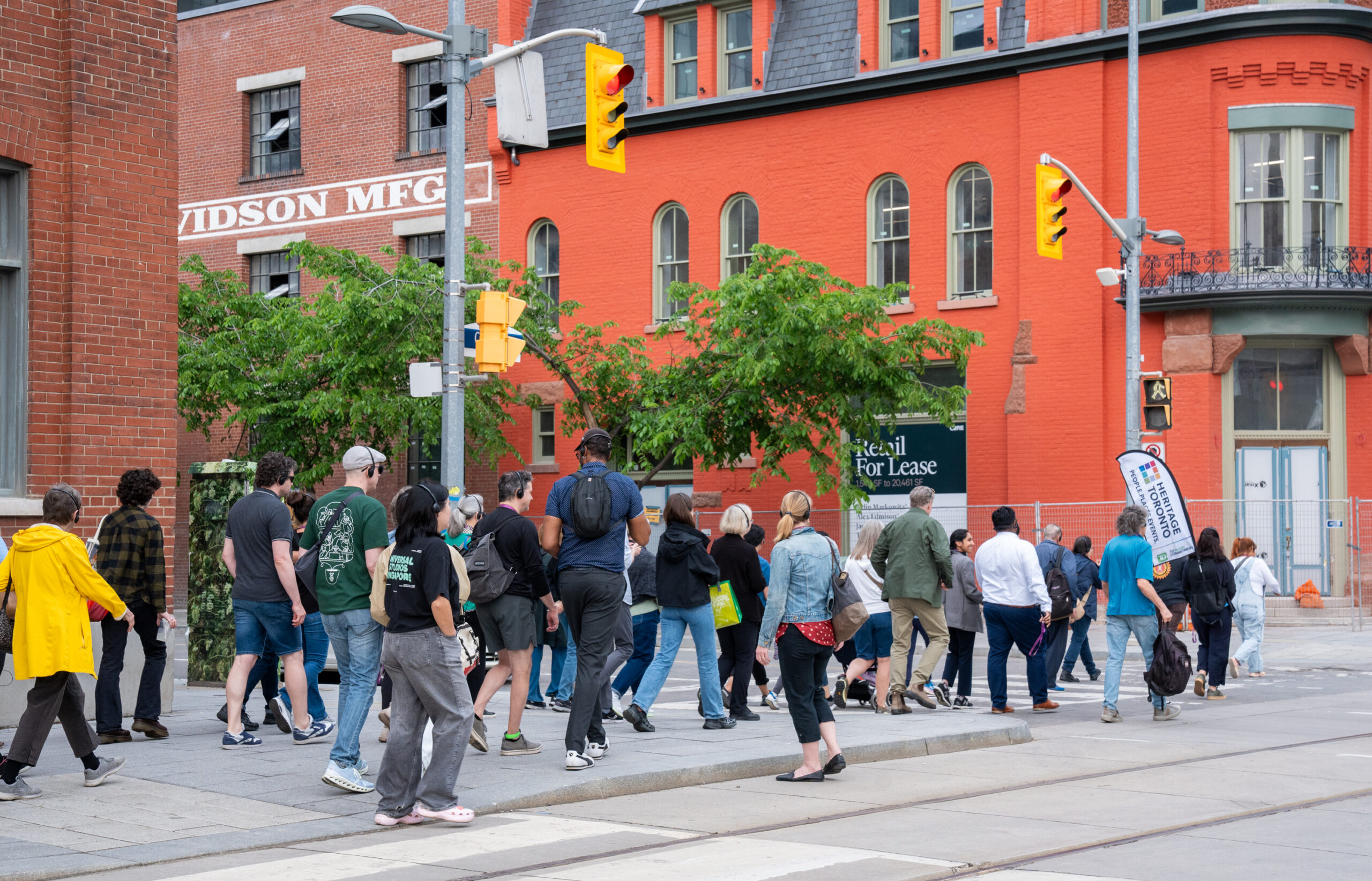 A group of people cross the street to reach a red-orange building.