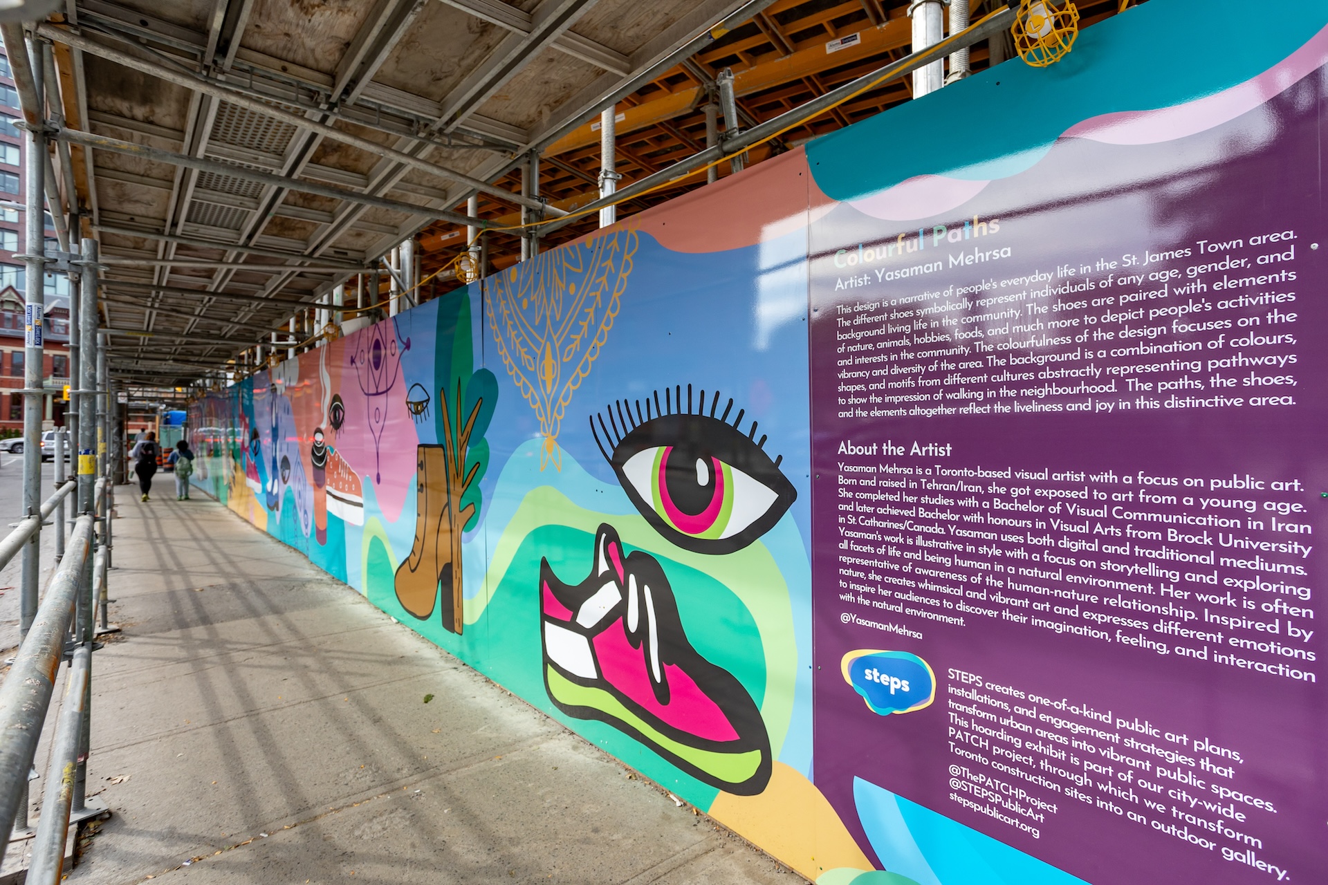 A colourful mural on a sidewalk wall with a large purple panel with written paragraphs.