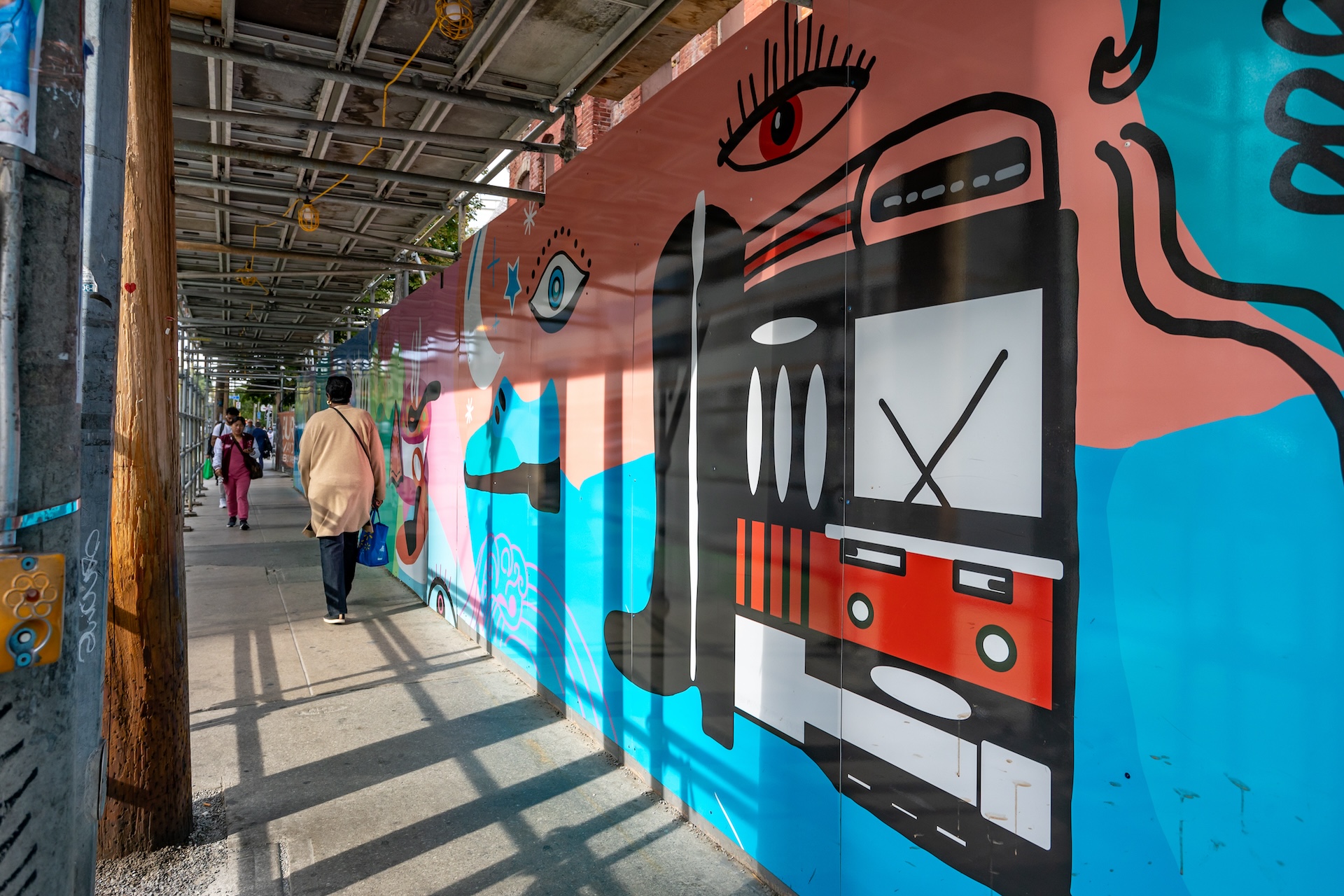 A colourful mural on a sidewalk wall with a streetcar, eyes, and abstract shapes.