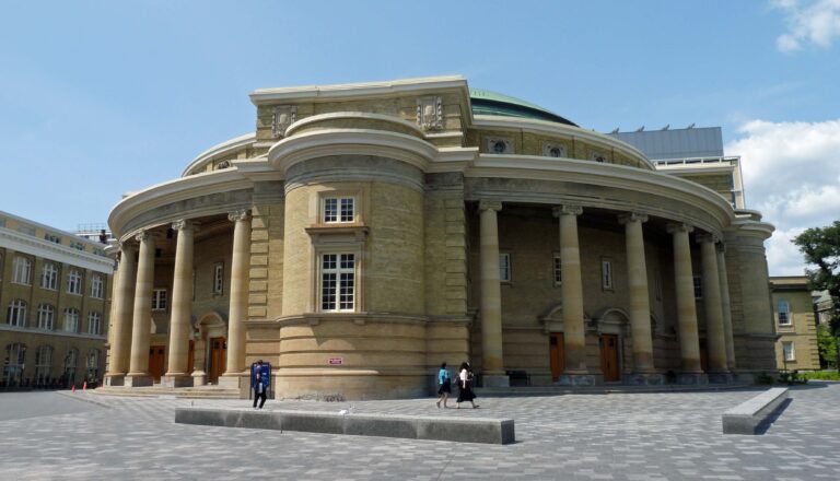 Large round yellow brick building with columns encompassing the structure on both sides.