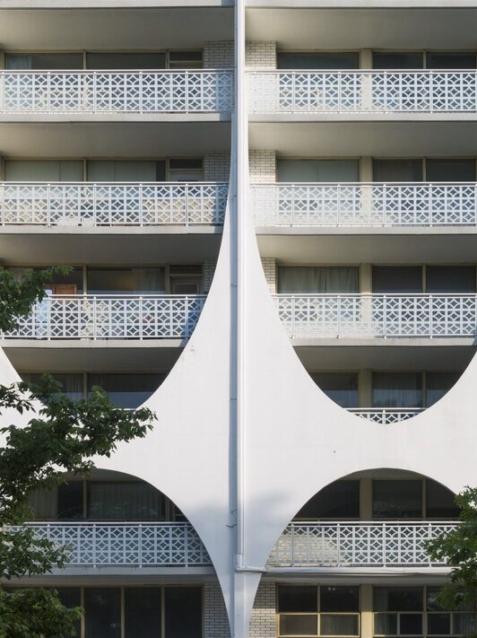 A zoomed-in photo of part of an apartment building. a number of balconies with white metal fencing are visible. Some balconies have white concrete obscuring our view of them.