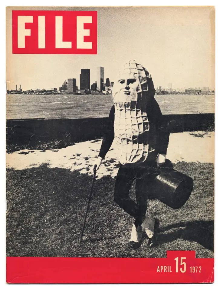 The front cover of a magazine. In the top left are the words "FILE" in large white letters on a red background. The main image is that of a person wearing a large peanut outfit, with a black top hat in their left hand and a cane in their right. In the distance a city skyline can be seen behind a large lake.