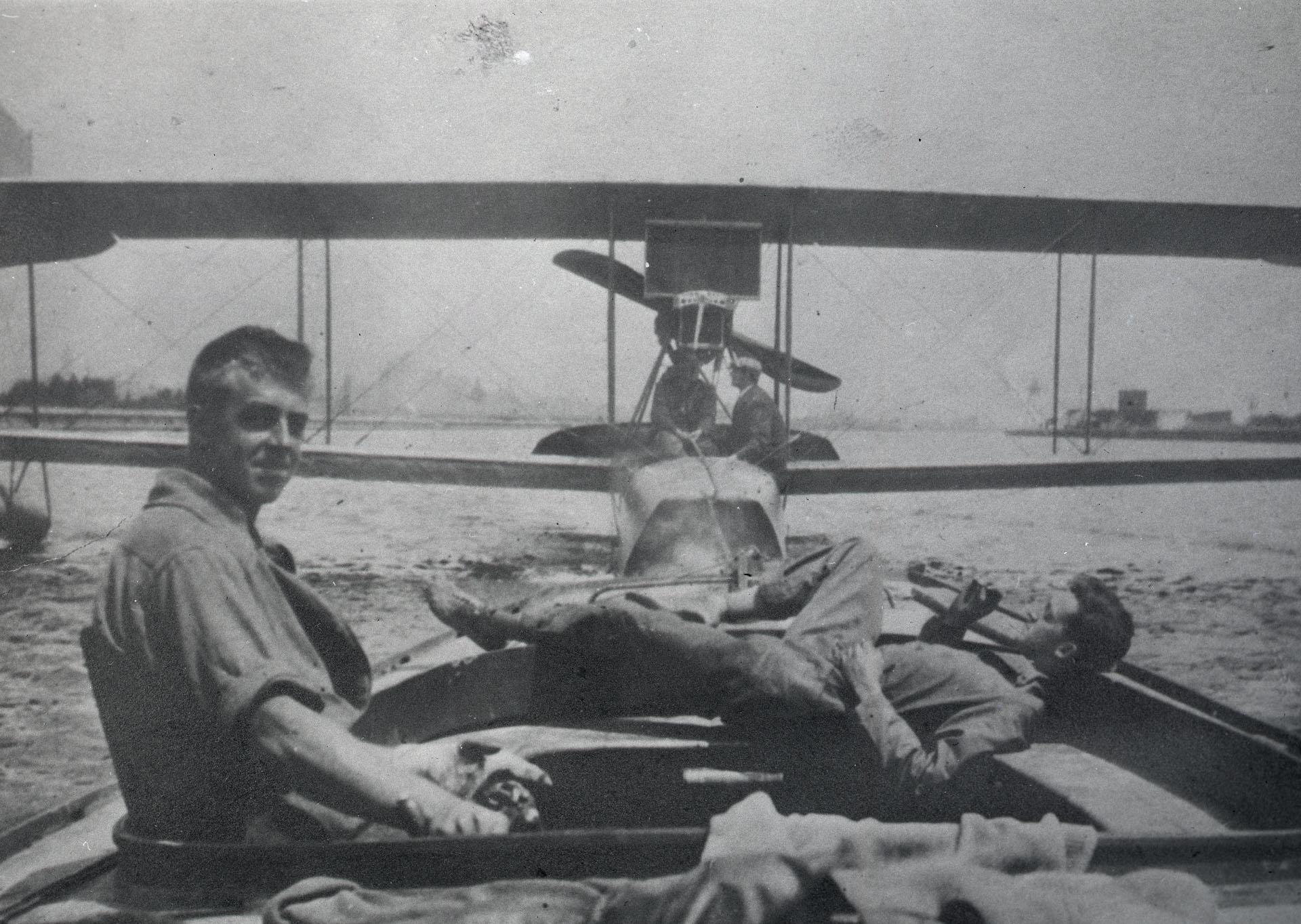 Black and white image of two men relaxing on a "flying boat" on the lake. The propeller and double wings are in the foreground of the image