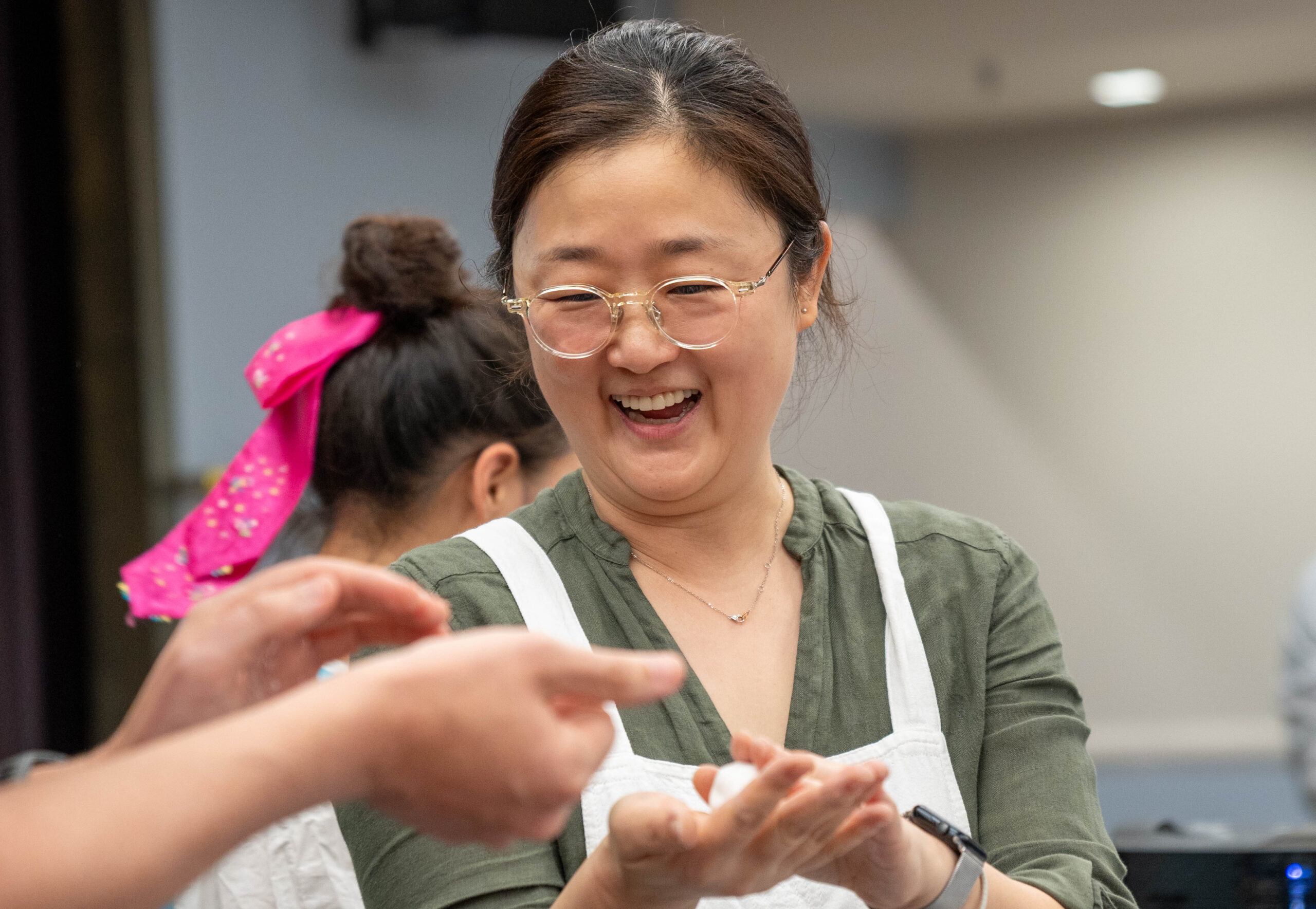 A woman wearing glasses and an apron holding dough.