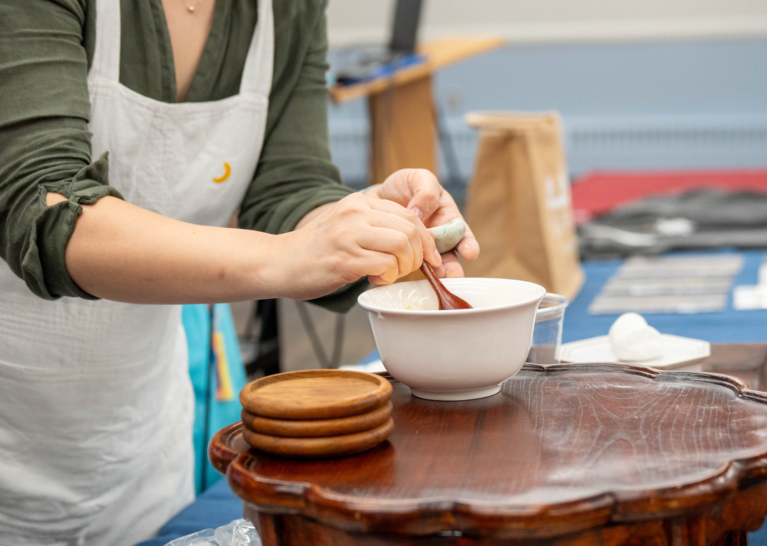 A hand of a person who wears an apron holding a spoon, taking songpyeon fillings from a bowl.