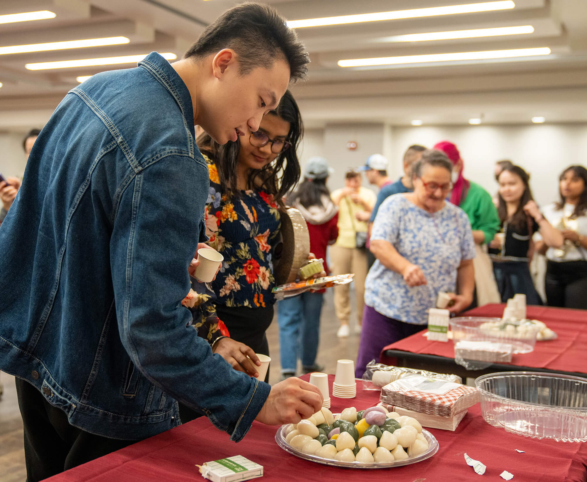 A man and woman use toothpicks to serve themselves. There is line behind them of people waiting for their turn to serve themselves food.
