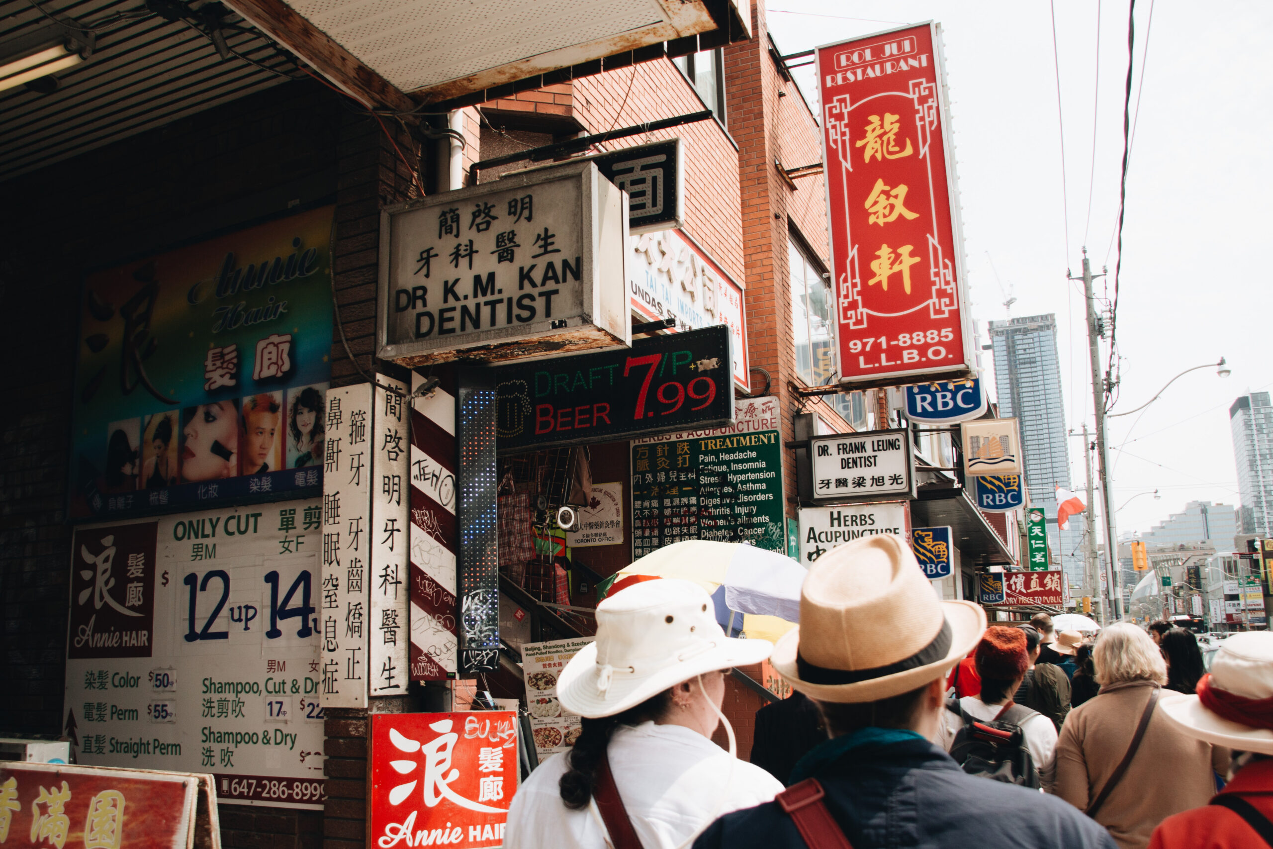 Group walks down street in Chinatown with storefront signs on left side.