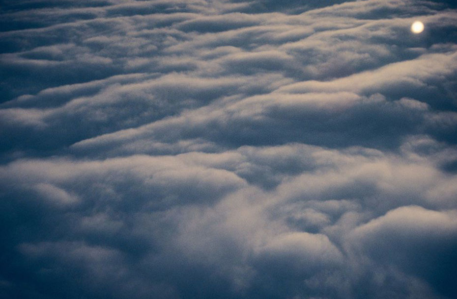 Colour photograph of a layer of clouds taken from above, most likely from the window of an airplane at sunrise or sunset.