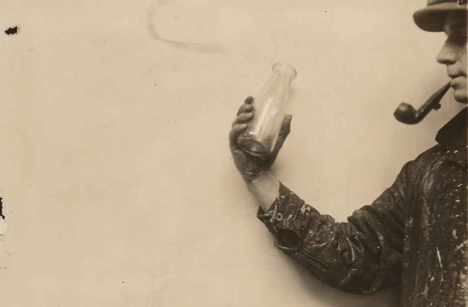 Sepia tone image on the right of which partially appears a man in profile, smoking a pipe. His right hand extends out into the centre of the image and holds and empty milk bottle.