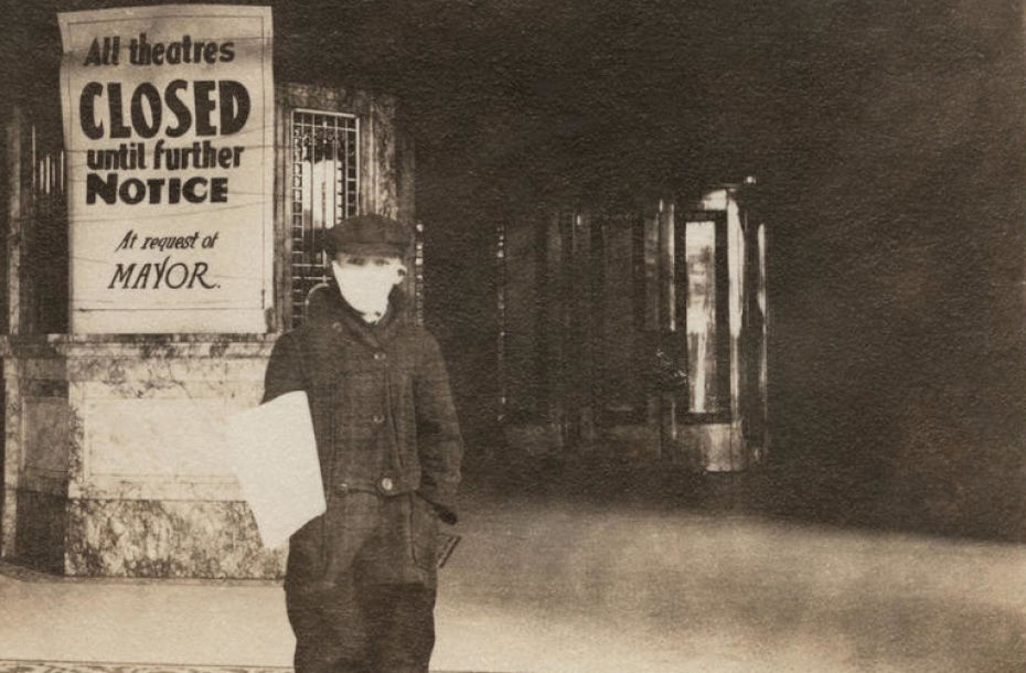 Sepia tone image of boy standing in front of a theatre entrance. He wears a mask. A sign posted on the box office reads - All theatres CLOSED until further notice. At request of Mayor