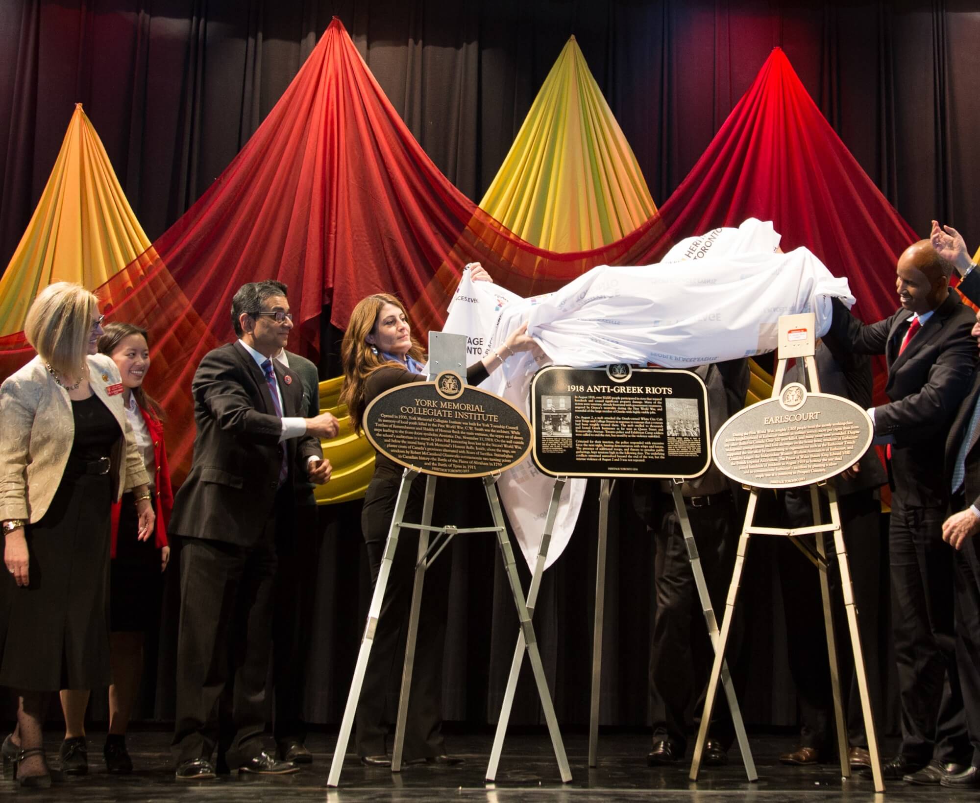 Ten persons on stage in the middle of unveiling three plaques.