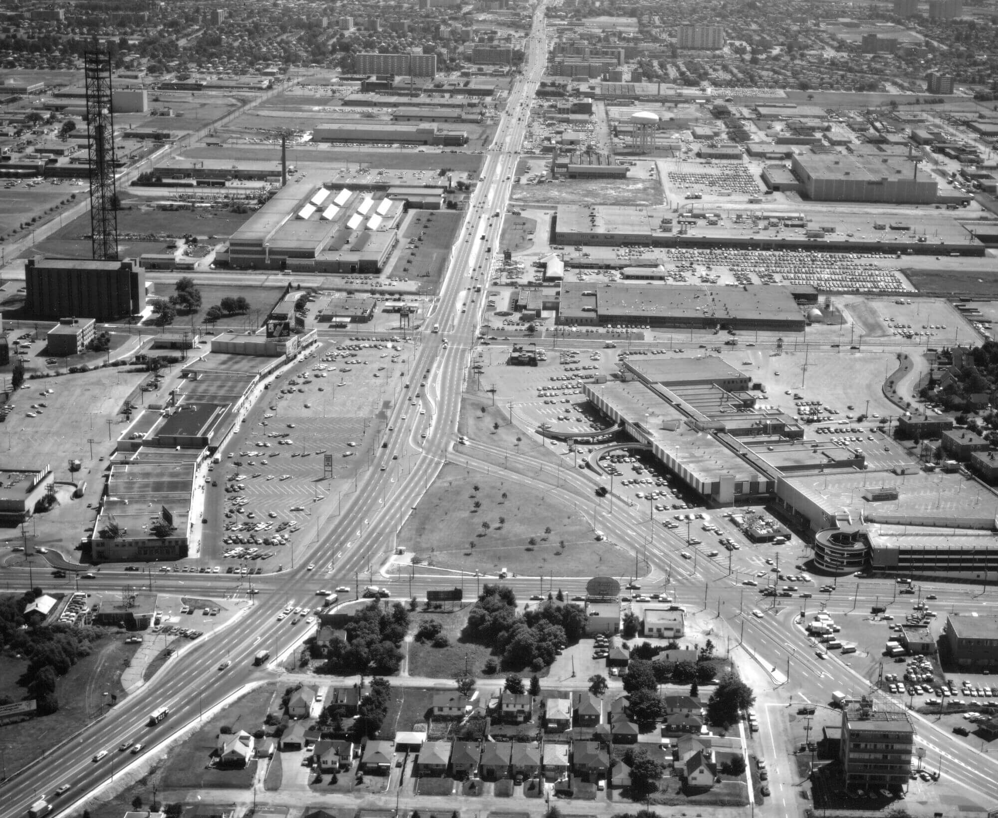 Black and white slightly aerial photograph looking east along Eglinton Avenue East through the Golden Mile from Victoria Park Avenue. Shopping plazas and surface parking lots cover the landscape.