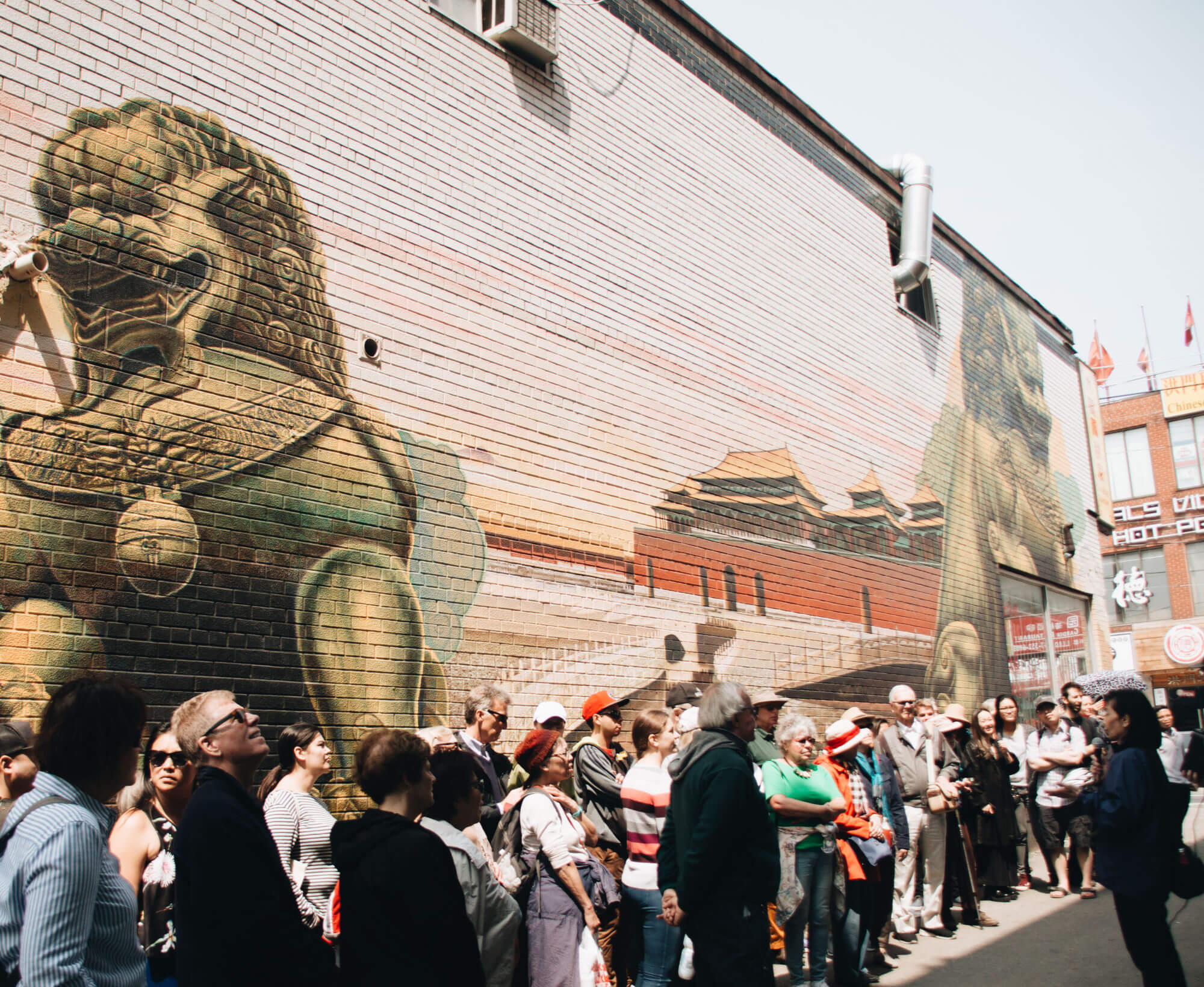 Group stands in alleyway in front of dragon mural listening to tour leader speak.