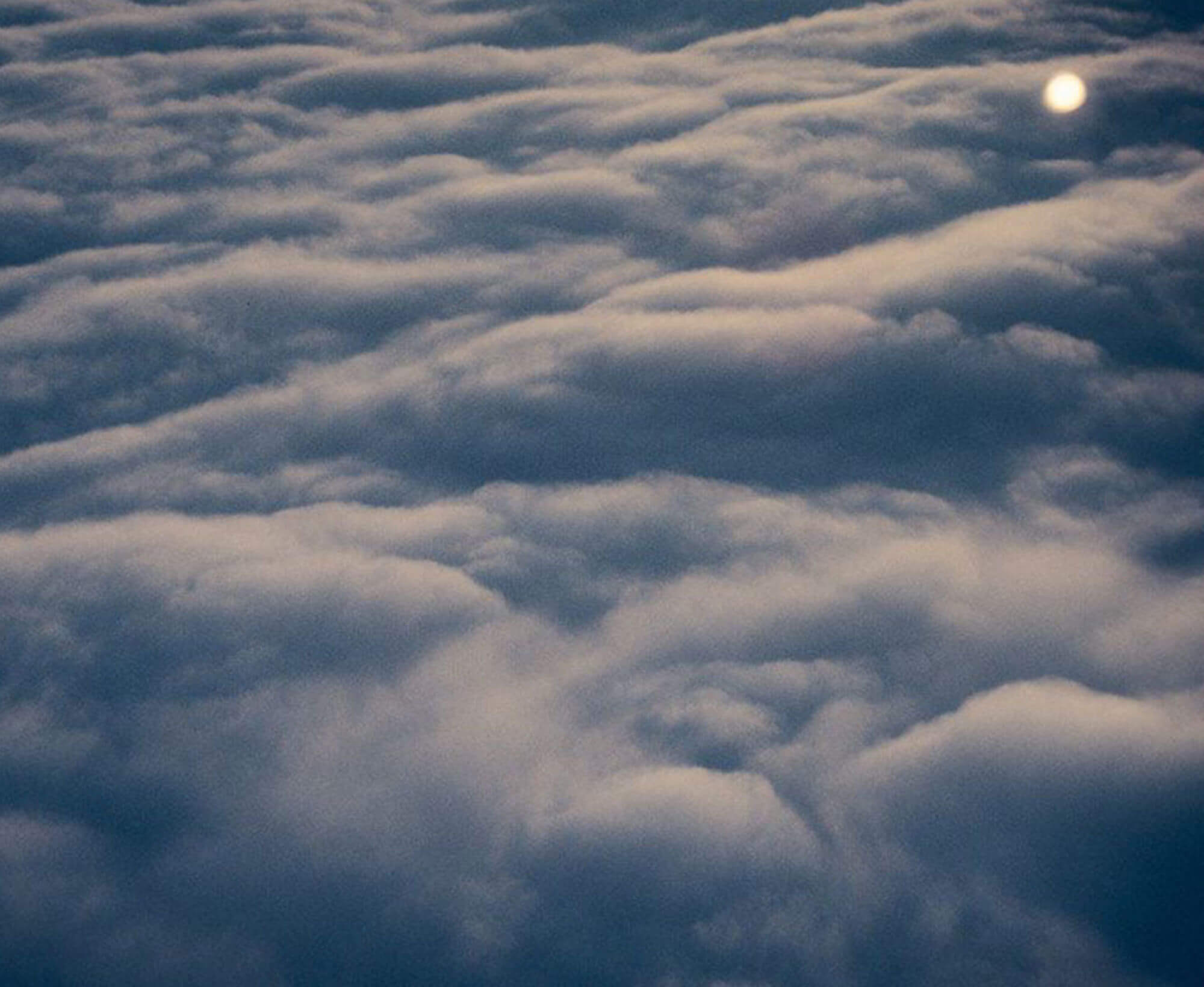 Colour photograph of a layer of clouds taken from above, most likely from the window of an airplane at sunrise or sunset.