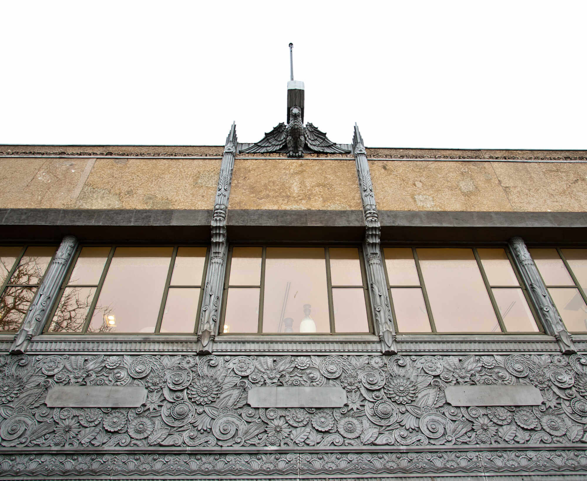 Closeup image of front facade of a building - looking up to the sky. Image shows a carved panel, row of windows, followed by row of being stone.