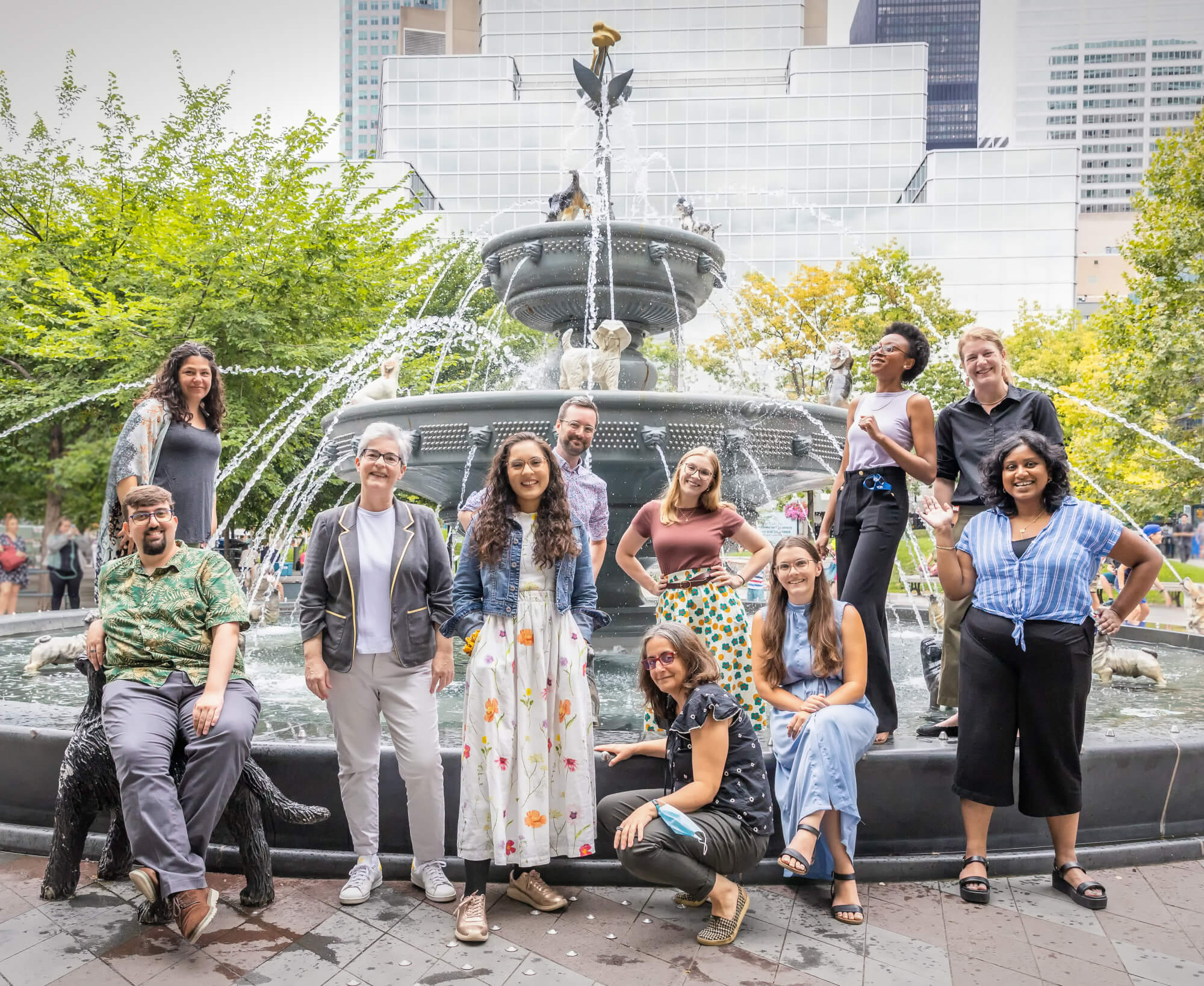 Group of people standing in front of a fountain in a park smiling at the camera.