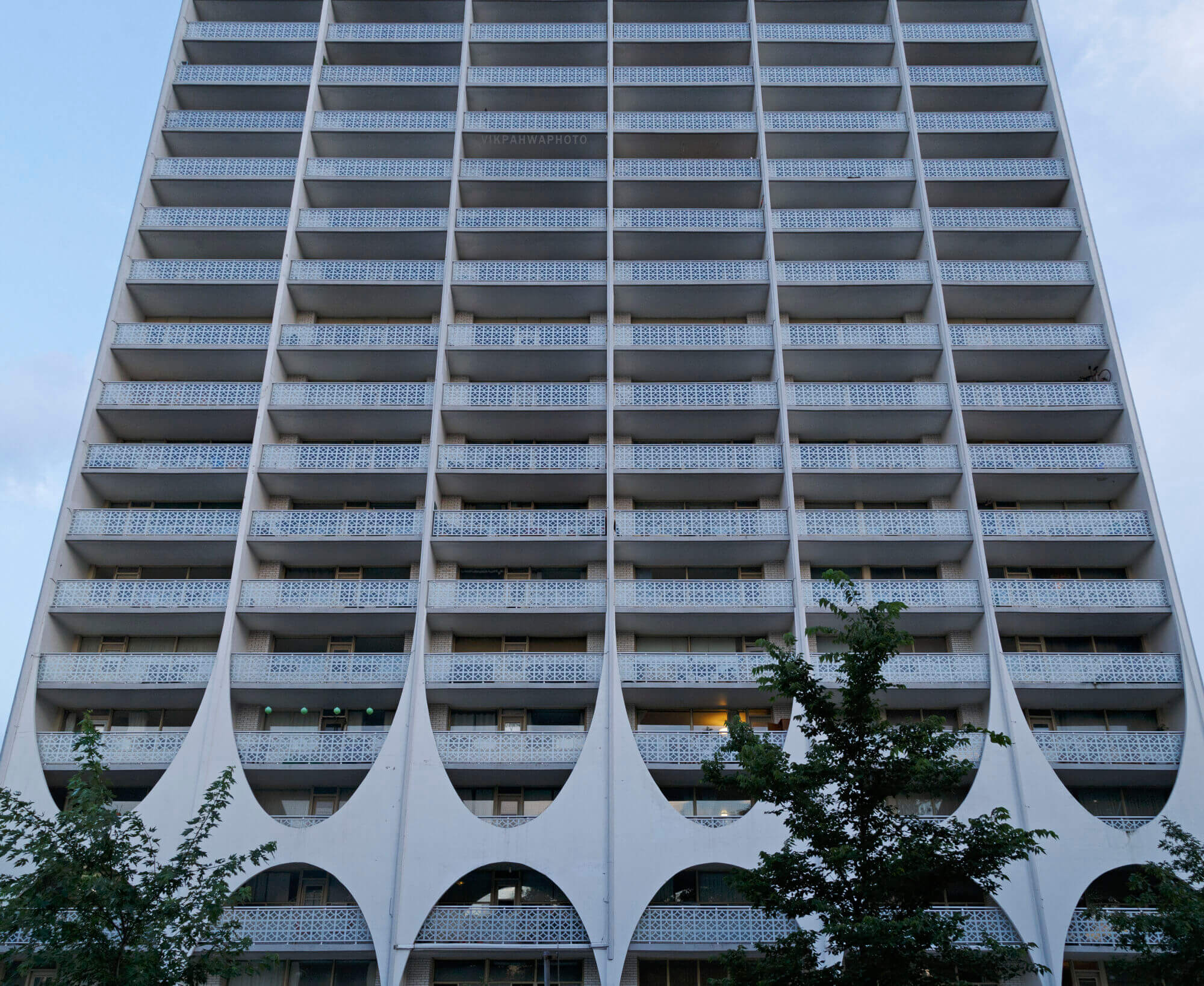 A large rectangular apartment building. Teh building is white and hads many windows and balconies.
