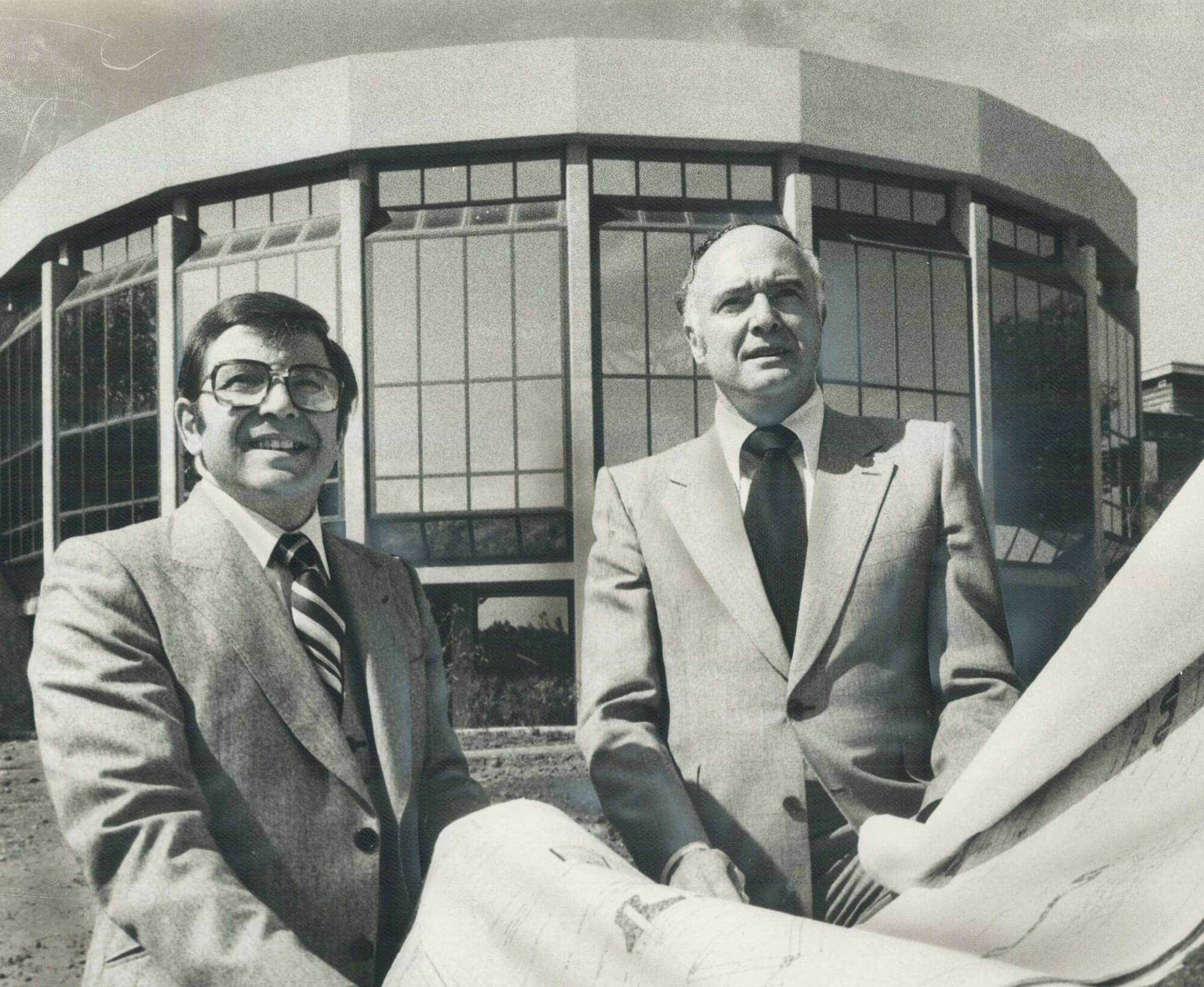 Two men holding architectural plans outside the nearly complete rotunda of the Columbus Centre