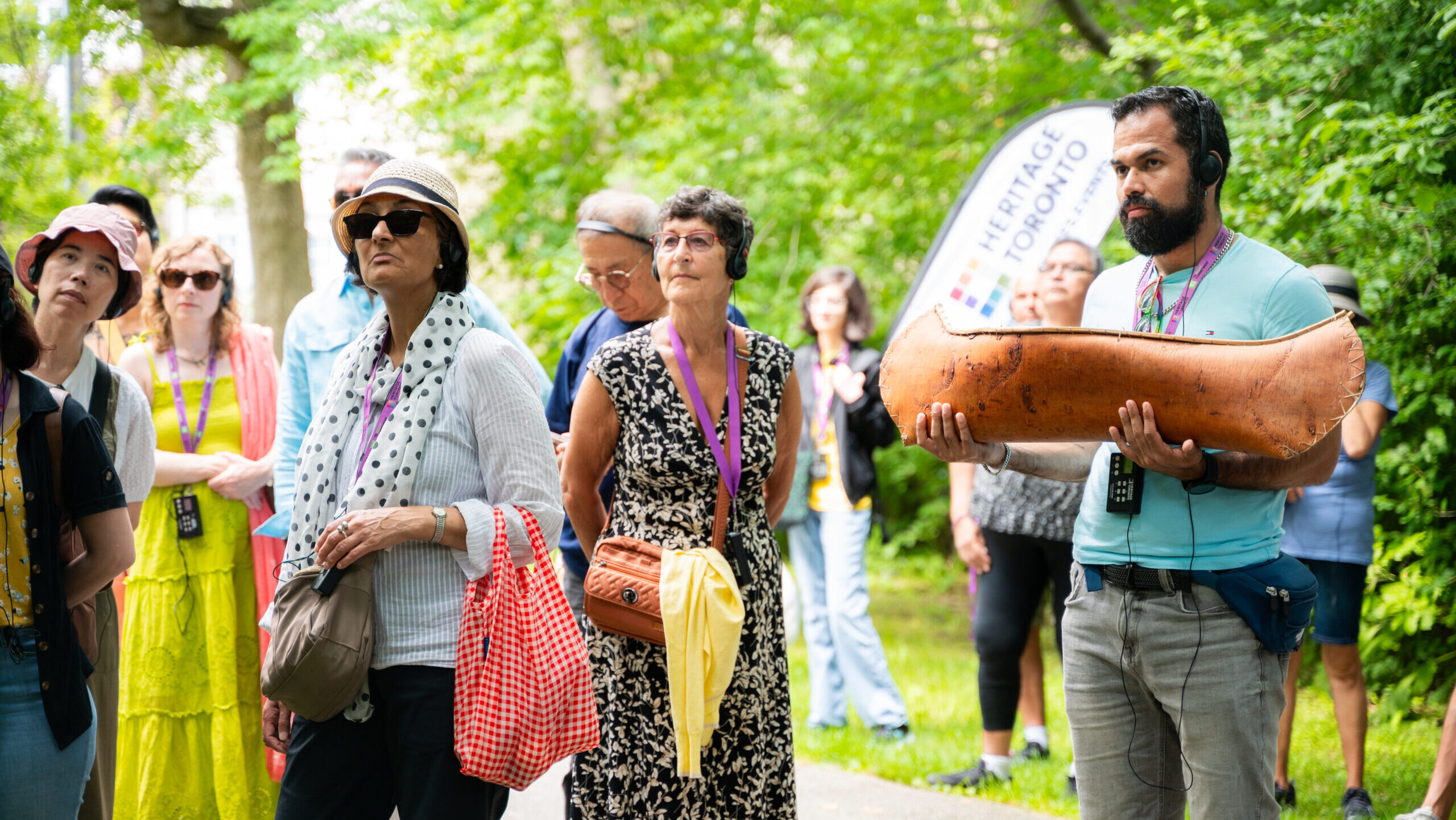 A tour group stands on the sidewalk in a park, one holds a miniature hand carved canoe.