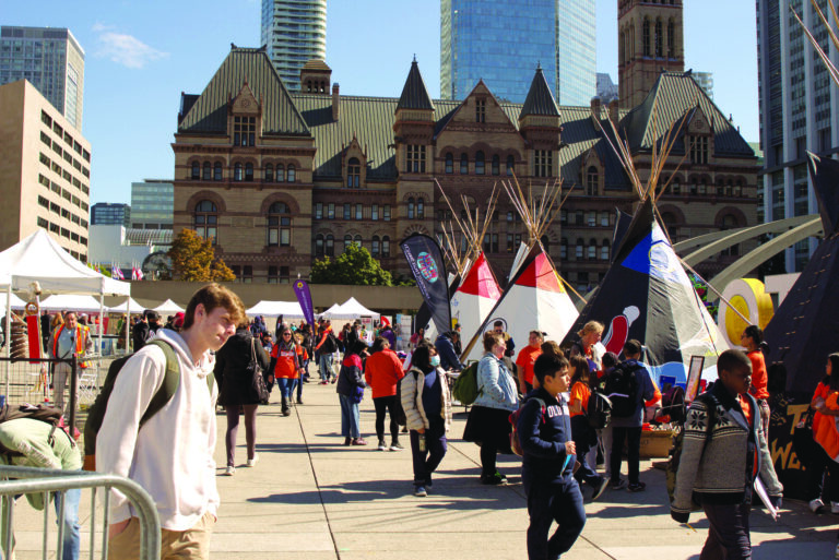 A large group of people involved in festivities. Three large tippis are surrounded by people.
