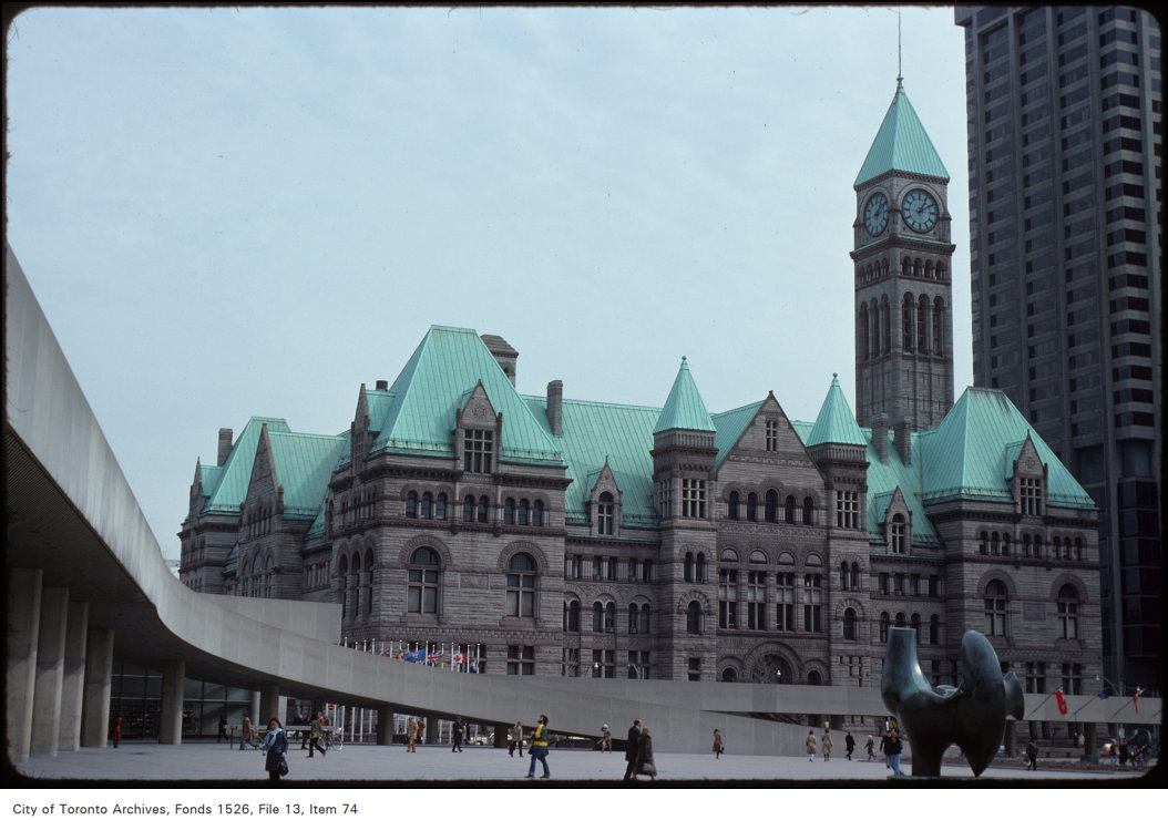 A large Victorian stone building with a green roof and clocktower (Old City Hall). In the foreground is the sweep of the concrete path connecting Nathan Phillips Square to the New City Hall.