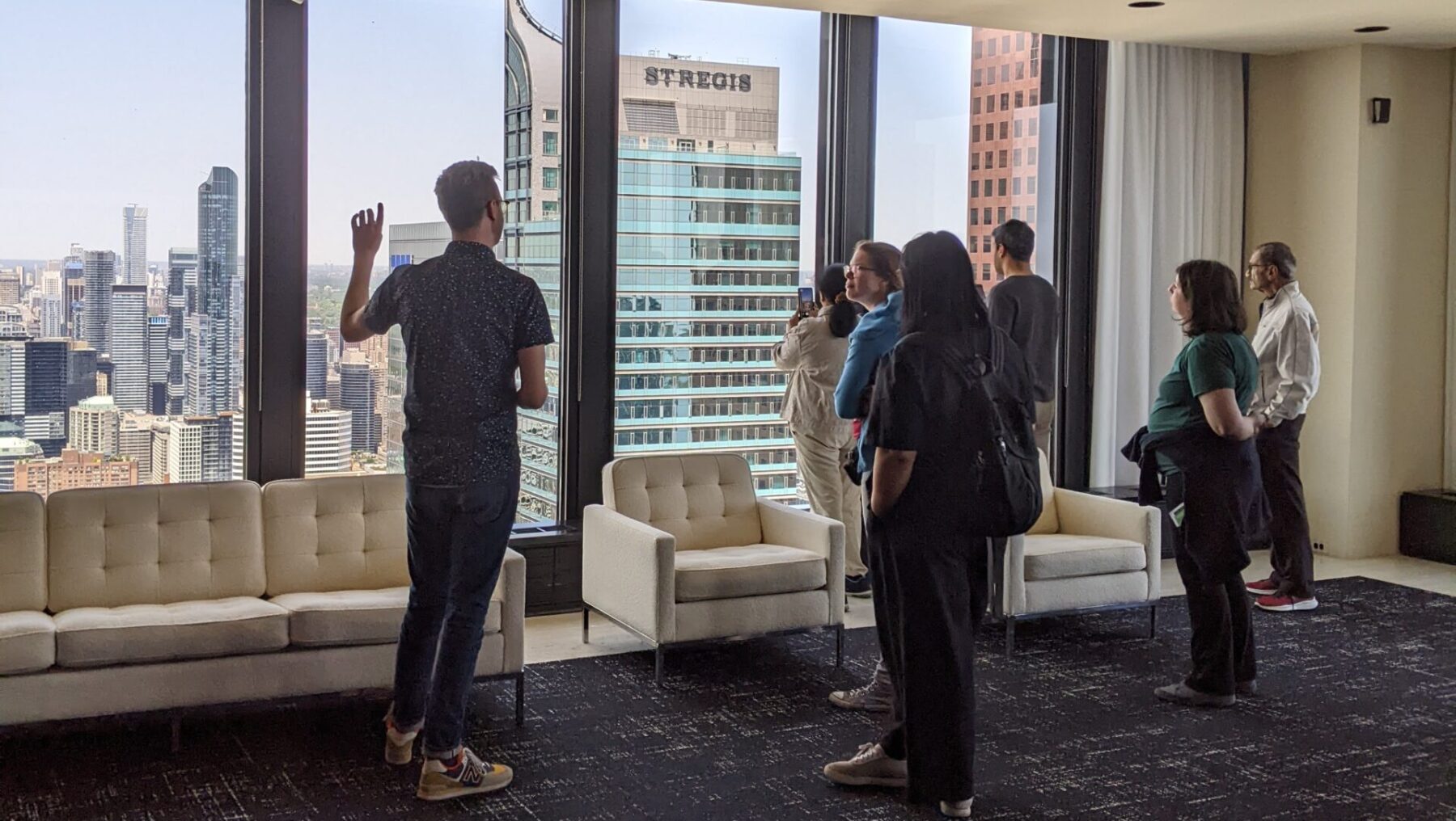 A group of people stand next to a large wall of windows looking out.