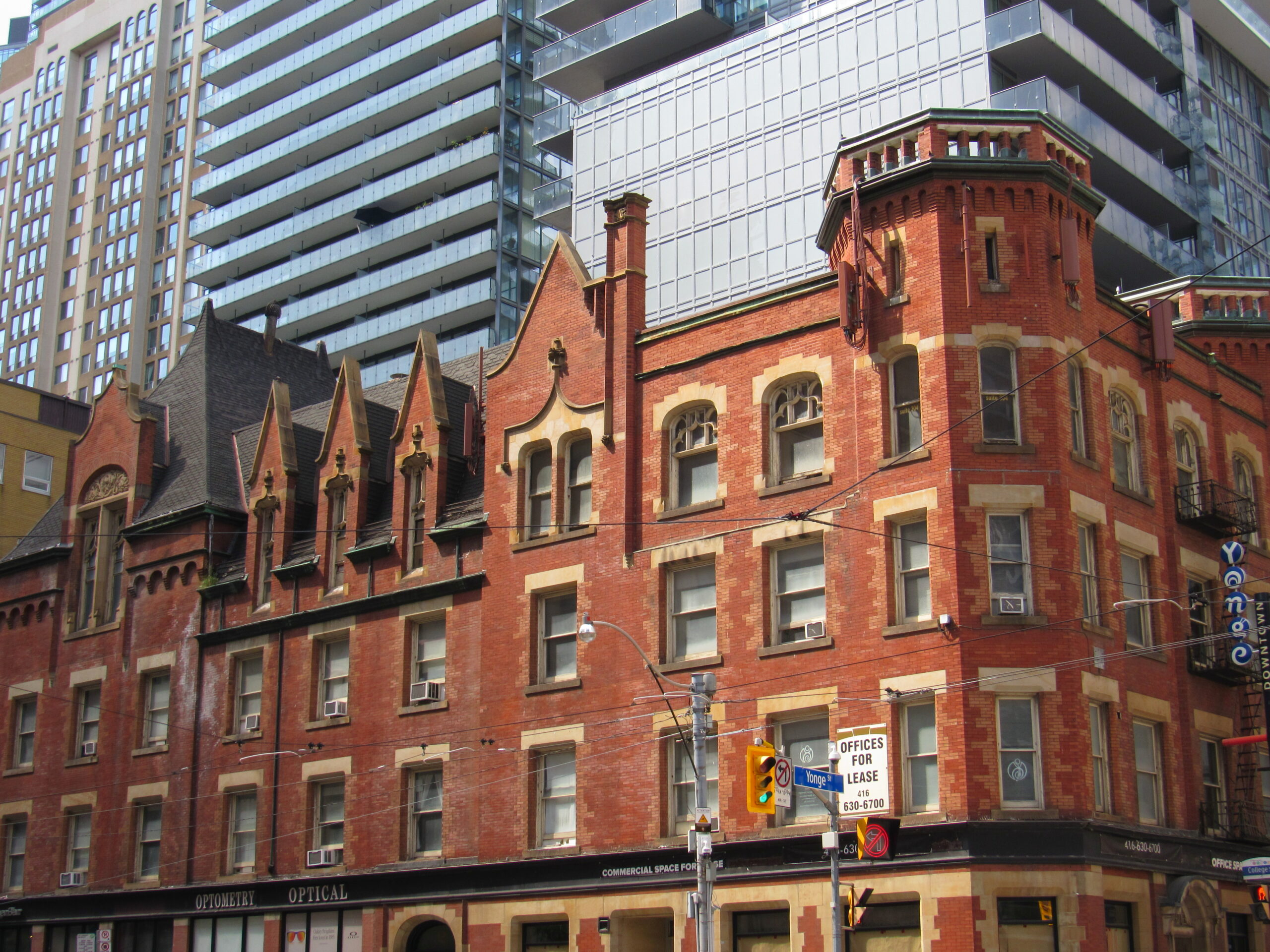 A four-storey red brick building stands in front of glass and steel skyscrapers.