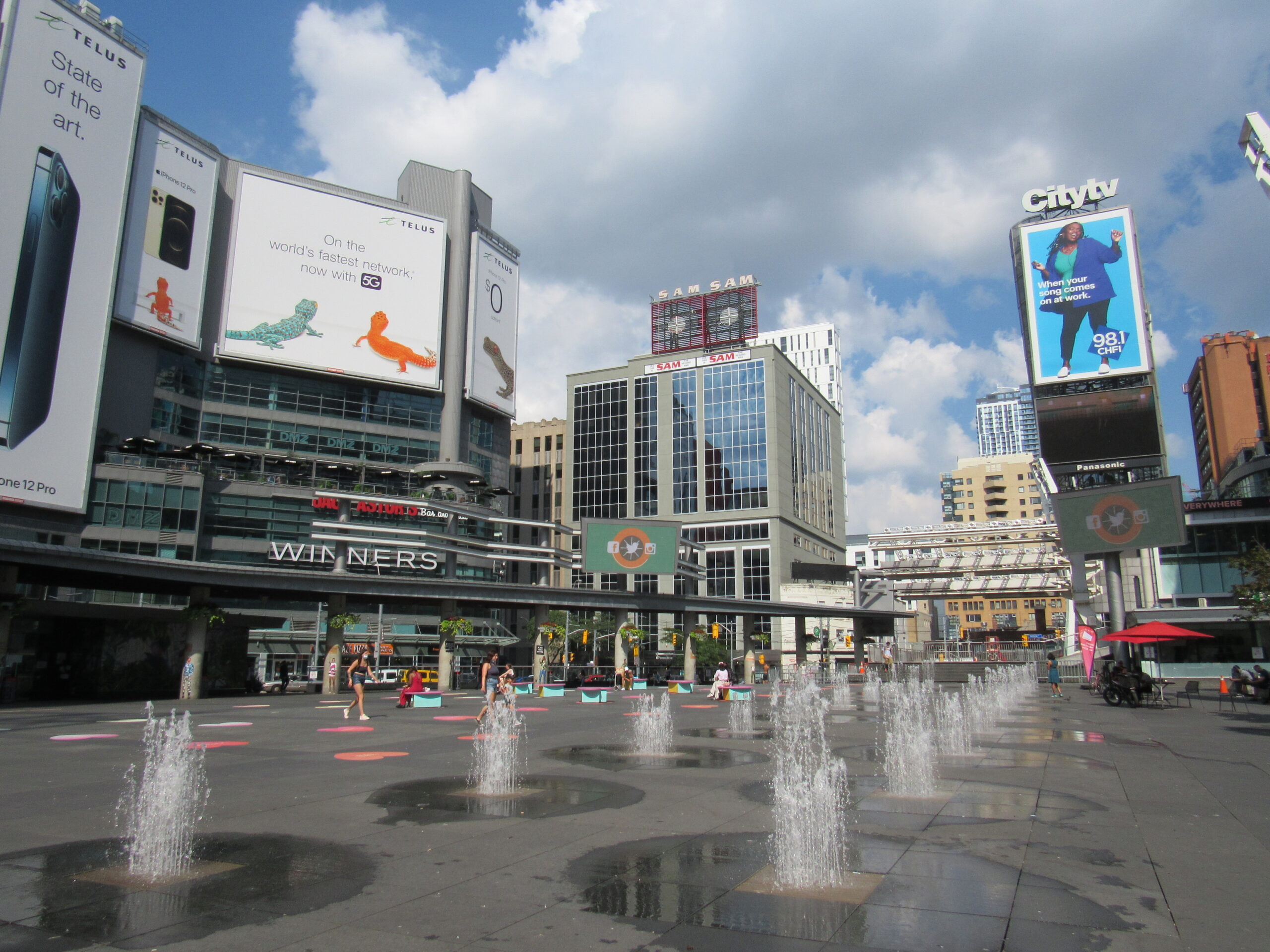 An empty street scene facing an open-air pavilion. Stores and skyscrapers surround the open paved area.