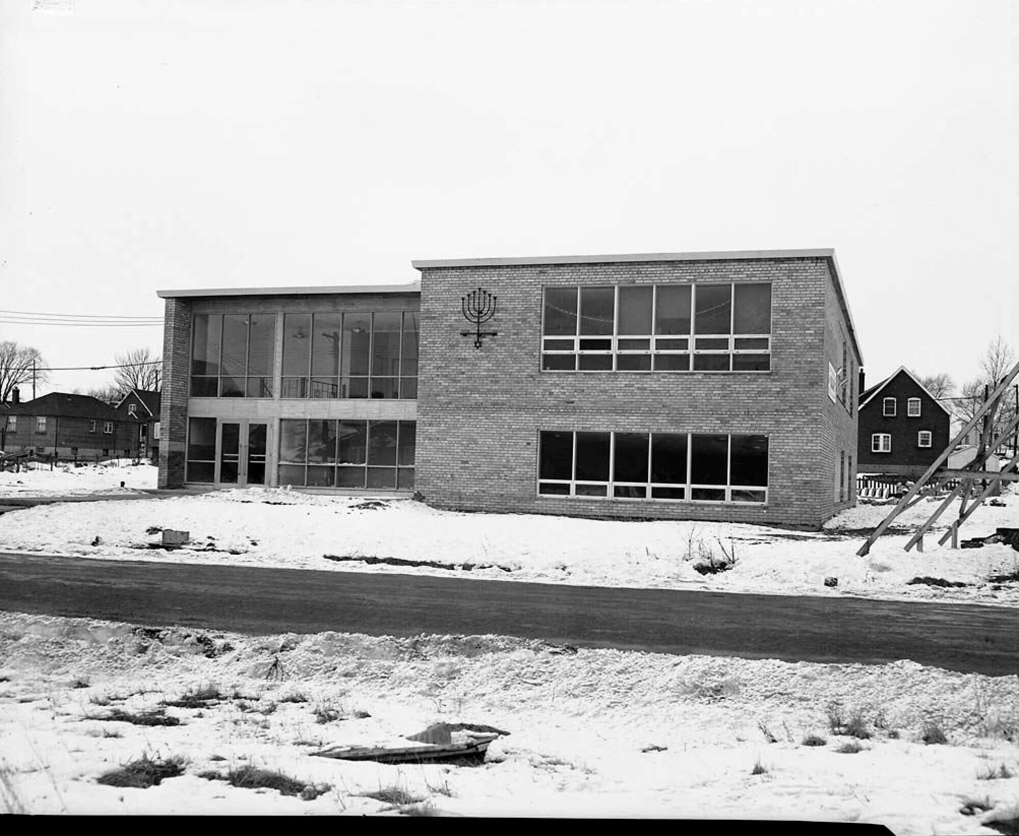 A two story building is photographed on a snowy day. The building has a sign shaped like a Mennorah.