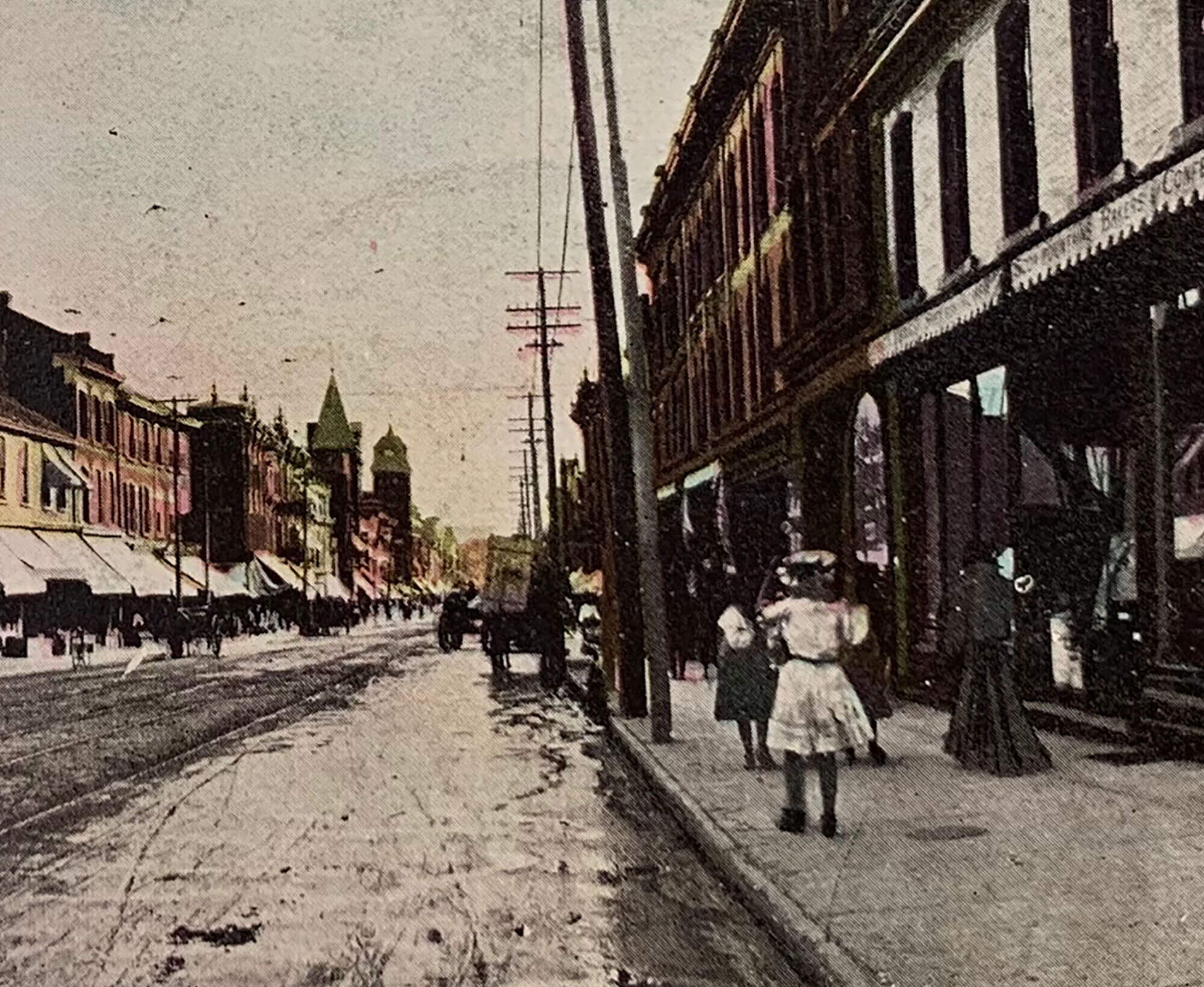 Panoramic photo of intersecting streets with commercial storefronts and small groups of people walking along the sidewalk.